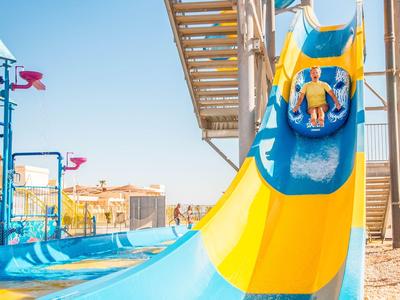 Kinder rutschen auf einer bunten Wasserrutsche in einem Wasserpark bei sonnigem Wetter.