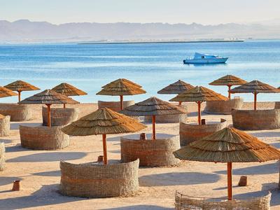 Strand mit mehreren Strohmachirmen und Sitzbereichen aus Stein am Meer.