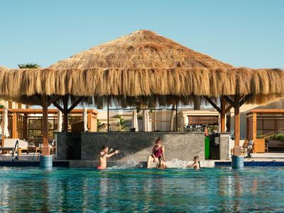 Poolbar mit Strohdach an einem Hotelpool bei klarem Himmel.