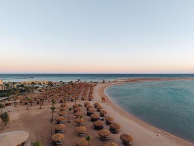 Strandhotel mit Reihen von Sonnenschirmen und klarem Meer bei Sonnenaufgang.