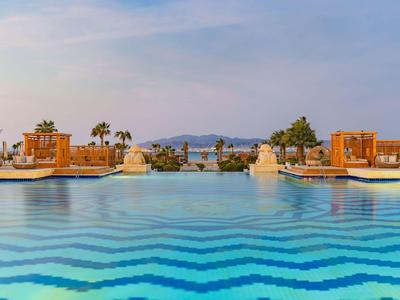 Großer Pool mit blauen Wellenmustern und Blick auf Palmen und Berge im Hintergrund.