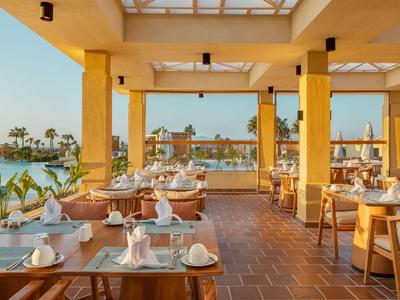 Offenes Restaurant mit Holztischen und Blick auf das Meer bei Sonnenuntergang.