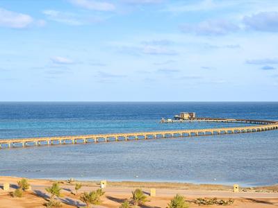 Geschwungener Steg mit Gebäude, das ins Meer ragt, unter blauem Himmel am Strand.