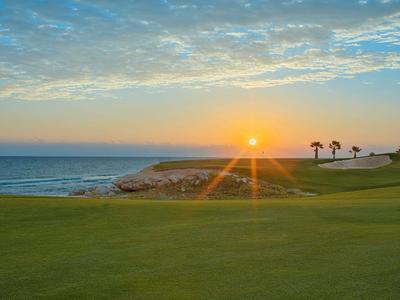 Sonnenuntergang über einem Golfplatz mit Meerblick und Palmen.