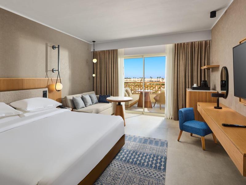 Modernes Hotelzimmer mit großem Bett, Sofa, Balkon und Fernsehgerät an der Wand.