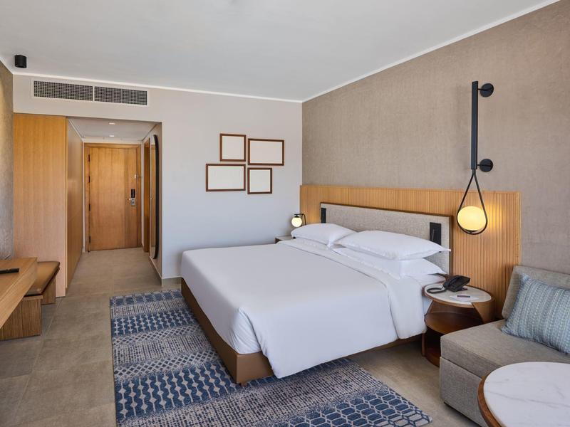 Modernes Hotelzimmer mit Doppelbett, Sofa, Teppichen und Holzmöbeln in hellen Farben.