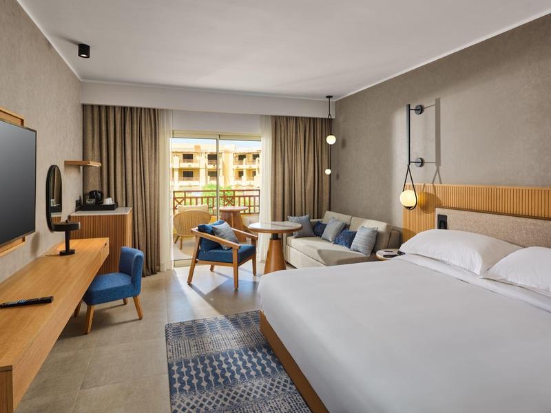 Modern eingerichtetes Hotelzimmer mit Doppelbett, Sofa, Schreibtisch und Balkon mit Blick ins Freie.