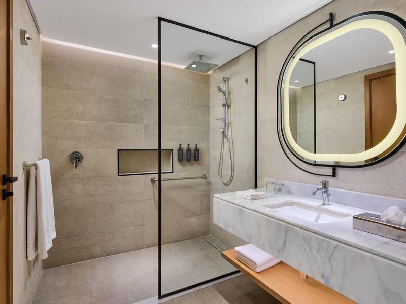 Moderner, heller Badezimmerraum mit begehbarer Dusche, rundem beleuchtetem Spiegel und Marmorwaschbecken.