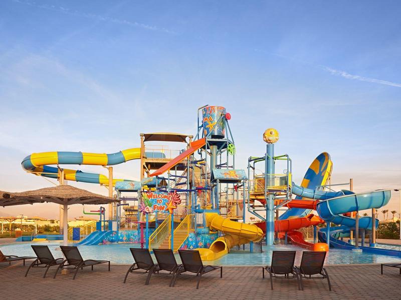 Wasserpark mit bunten, großen Wasserrutschen und mehreren Becken unter blauem Himmel.