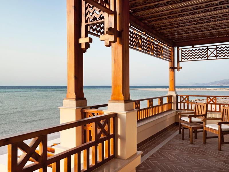 Balkon mit Holzmöbeln und Veranda, Blick auf ruhiges Meer und blauen Himmel.