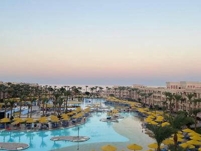Großer Hotelpool mit Palmen und Sonnenschirmen bei Sonnenuntergang.
