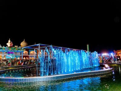 Beleuchteter Springbrunnen in Blau mit Menschen und Gebäuden im Hintergrund bei Nacht.