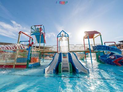 Wasserpark mit mehreren bunten Rutschen, Wasserfällen und flachem Pool bei sonnigem Himmel.