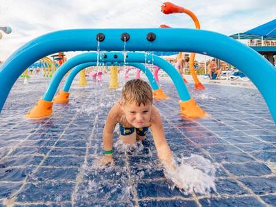 Kleiner Junge spielt fröhlich unter blauen Wasserspritzbögen auf nassem Boden.