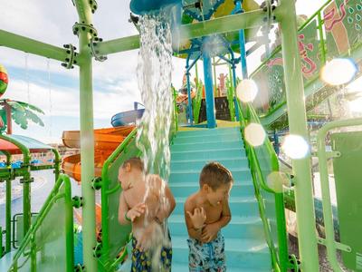 Zwei Kinder stehen unter Wasserfall in buntem Indoor-Wasserspielplatz.