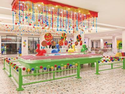 Bunte Indoor-Spielecke mit großen Lutscher-Dekorationen und glänzenden Murmeln am Boden.