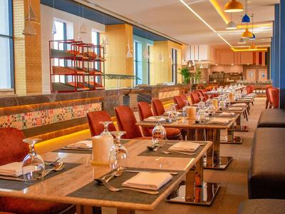Modernes Restaurant mit Holz- und Ledermöbeln, langen Tischen, Stühlen und warmem Lichtambiente.