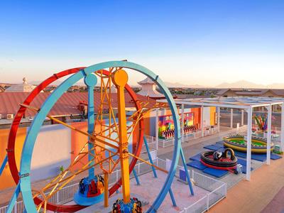 Bunte Freizeitpark-Attraktionen mit Achterbahn und Karussell unter klarem Himmel bei Sonnenuntergang.