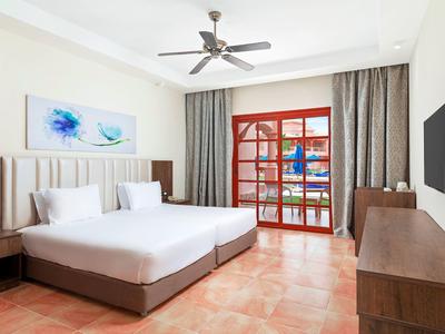 Helles Schlafzimmer mit großem Bett, Deckenventilator, bodentiefen Fenstern und holzfarbenen Möbeln.