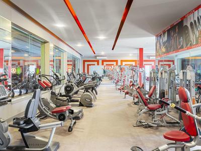 Großer, heller Fitnessraum mit zahlreichen modernen Trainingsgeräten und roten Akzenten an Decke und Sitzen.