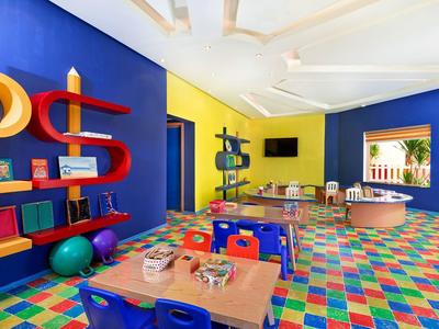Buntes Klassenzimmer mit blau-gelben Wänden, farbigem Boden und Tischen mit Spielzeug und Büchern.