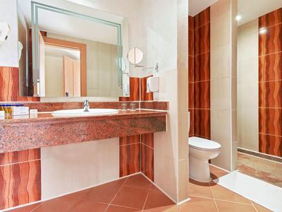 Helles Badezimmer mit rotem Marmorwaschtisch, großem Spiegel und Dusche, WC neben abgetrennter Wand.