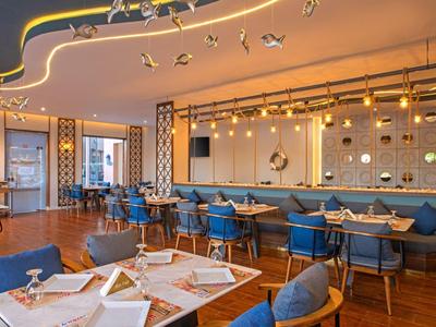 Modernes Restaurant mit blauen Stühlen, Holztischen und stilvoller LED-Beleuchtung an der Decke.