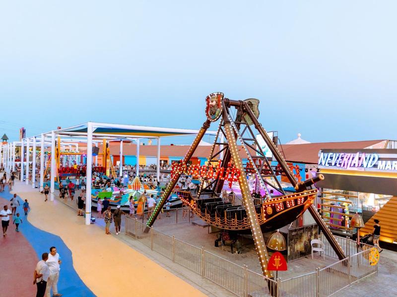 A covered leisure area featuring a hanging ship ride surrounded by people.