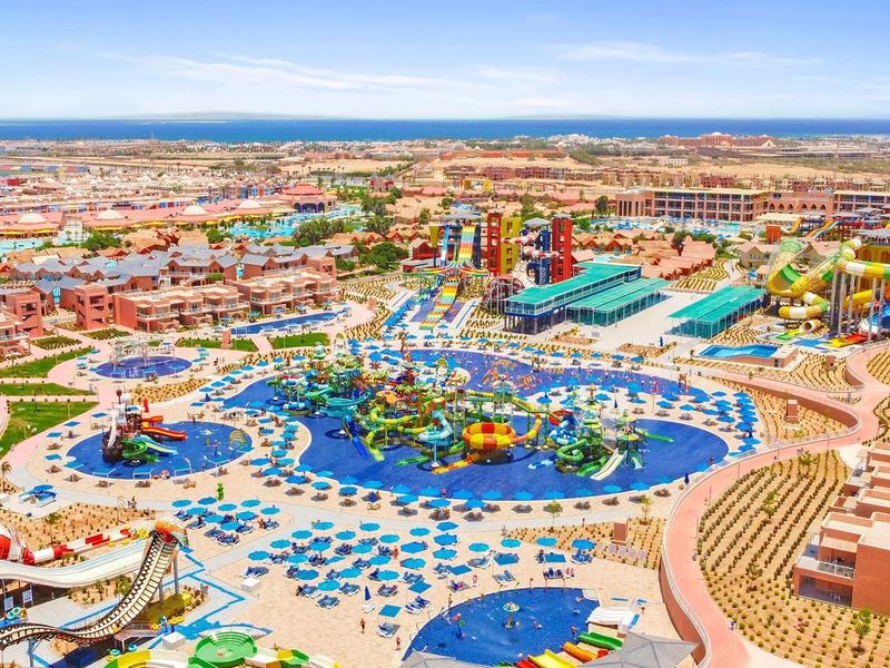 Large water park with pools, slides, and lounge chairs under clear blue sky.