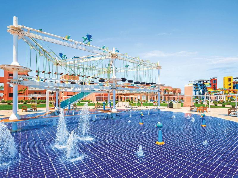 Hotel outdoor area with water pool, fountains, and climbing structure under clear sky