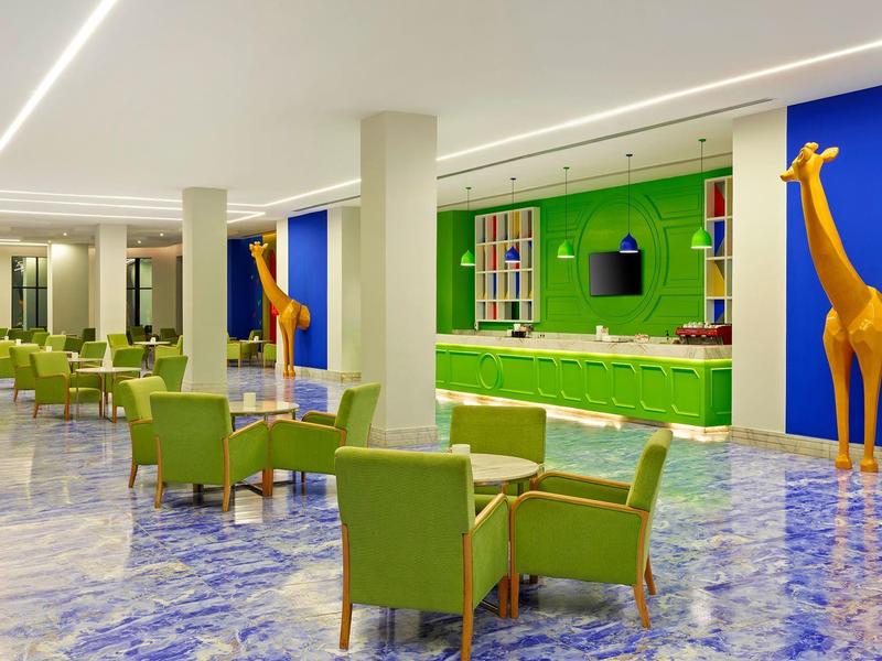 Hotel lobby with green chairs, blue and green walls, and giraffe statues near the bar area.