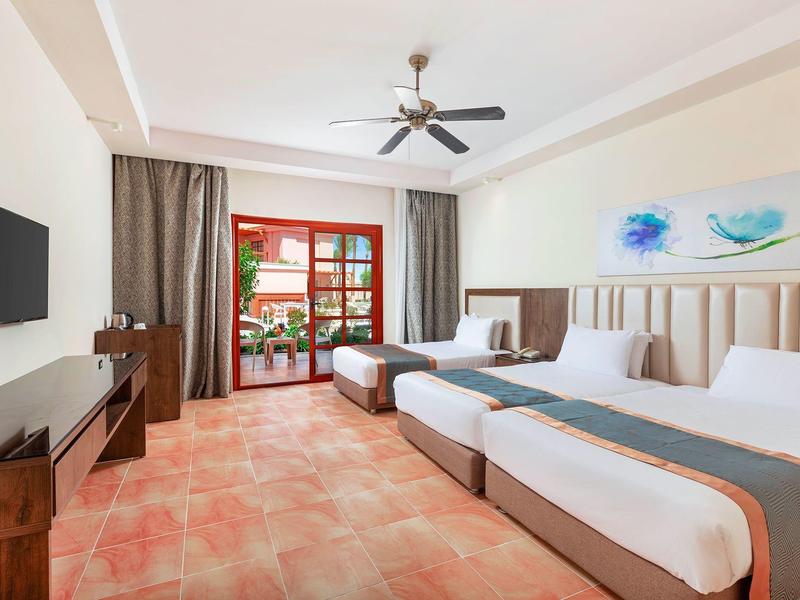 Hotel room with two beds, ceiling fan, TV, and balcony door with curtains.