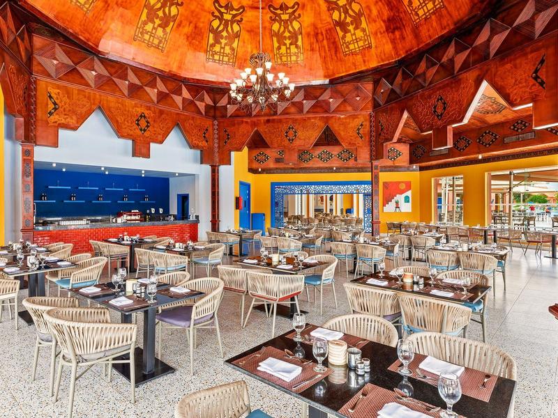 Spacious restaurant with round tables, wicker chairs, and a warm, decorated ceiling.