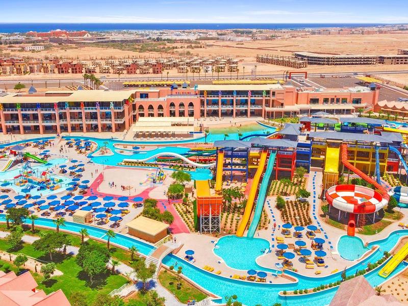 Large resort with multiple pools, water slides, sun umbrellas, and sandy desert surroundings.