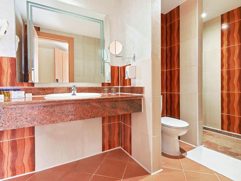 Modern bathroom with red tile accents, large mirror, sink, and toilet next to shower area.