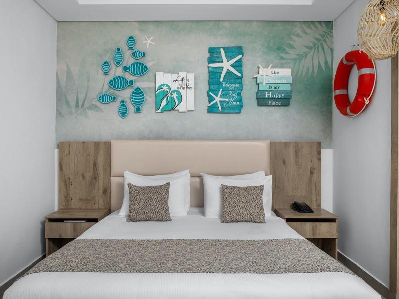 A modern hotel room with a double bed, wooden furniture, and nautical wall decor.