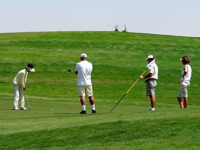 Quattro persone giocano a golf su un campo verde sotto un cielo limpido.
