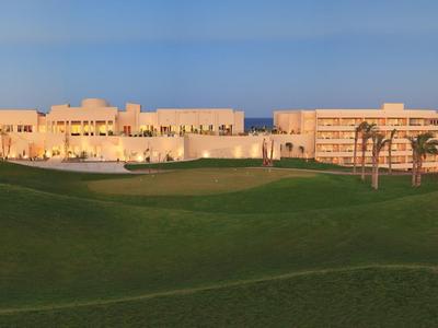Large hotel building beside a wide green golf course under a clear blue sky.