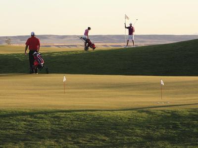 Golfers playing on a green course during sunset with hills in the background.