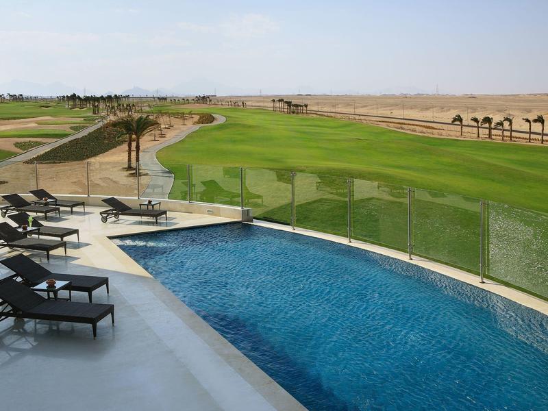Outdoor pool with lounge chairs overlooking a green golf course under a clear sky.