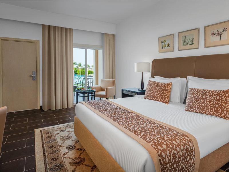 Modern hotel room with a large bed, patterned pillows, bedside lamp, and a window with curtains.