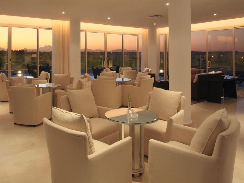 Hotel lounge with beige armchairs and glass tables during sunset.