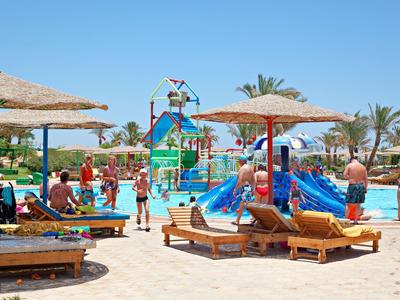 Children playing in a sunny pool area with water slides and lounge chairs under parasols.