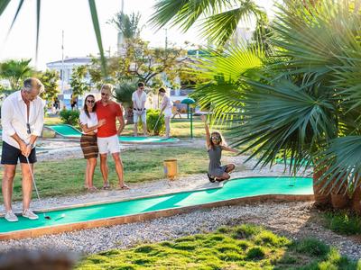 People playing mini golf in a sunny outdoor area surrounded by palm trees.