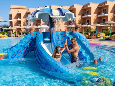 Children and an adult at the blue water slide playground in a hotel pool.