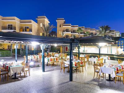 Evening outdoor view of a lit hotel with set tables under pergolas.