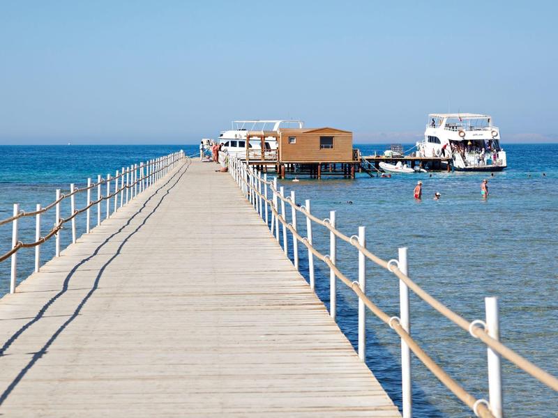 Holzsteg führt zu einem Haus und Boot im klaren blauen Meer unter blauem Himmel.