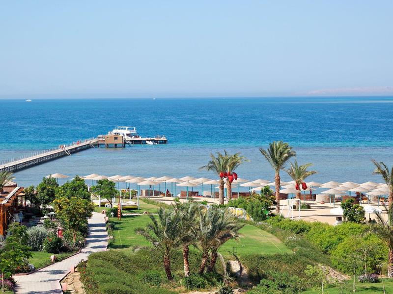 Strand mit Sonnenschirmen, Palmen und Steg, der ins blaue Meer führt