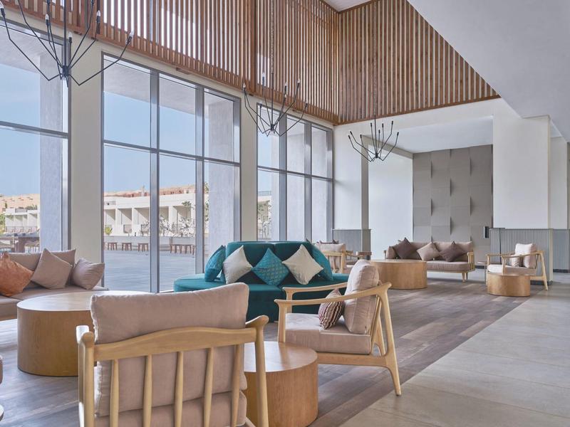 Großzügiger Hotellounge-Bereich mit hohen Fenstern, modernen Möbeln und viel Tageslicht.