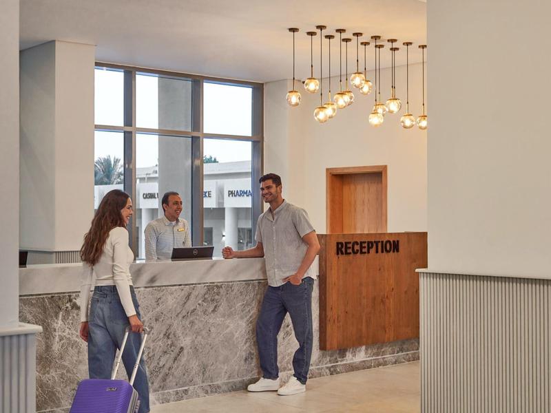 Hotelrezeption mit Empfangspersonal und Gästen mit Gepäck im modernen Eingangsbereich